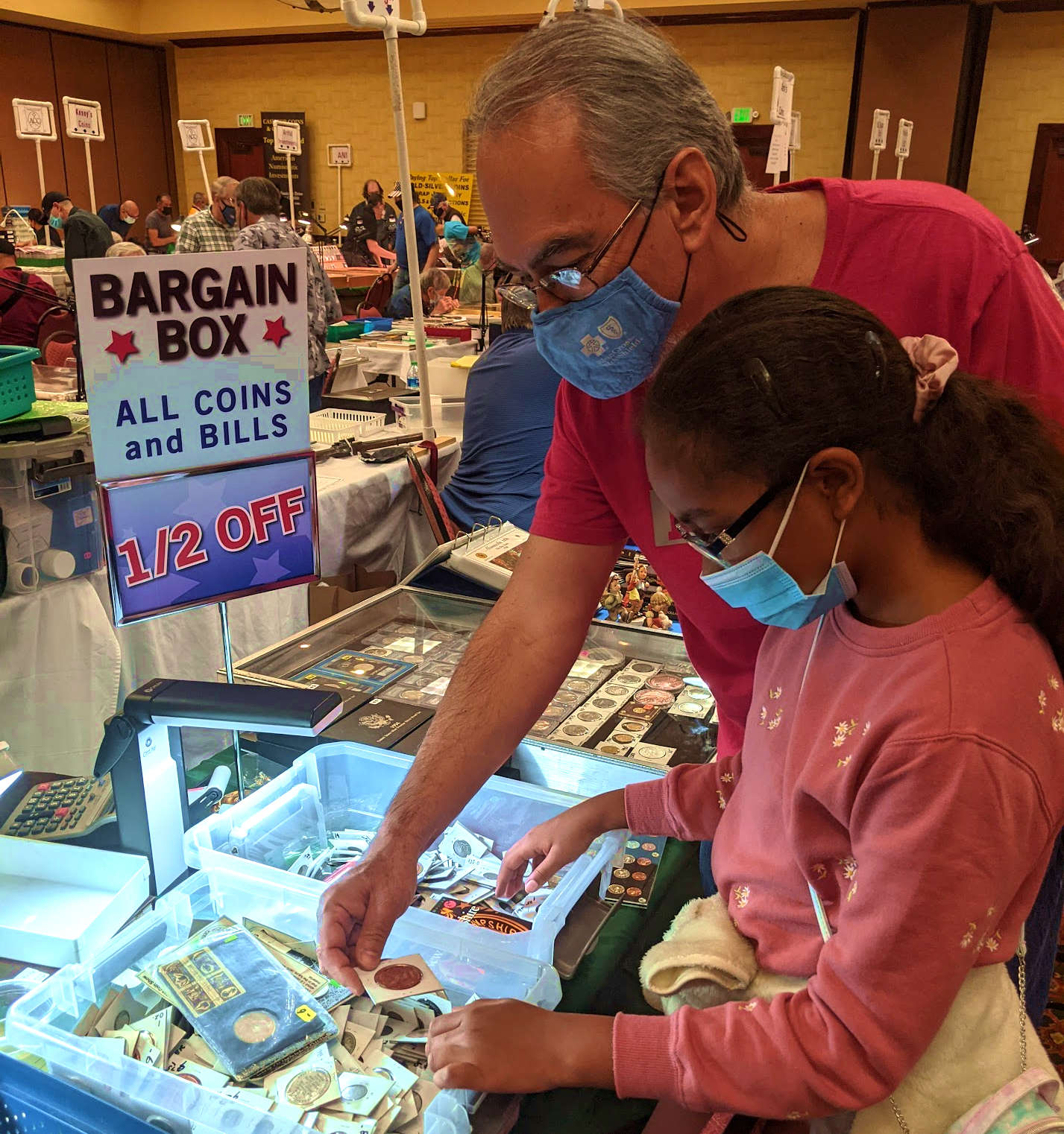A young girl and her father looking for coins in a bargain bin
